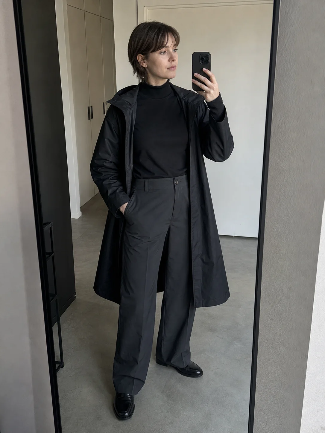 Copenhagen hallway mirror styling image showing the Clothixpack CXP-H101 Pivot Mock Neck Shirt tucked into slate trousers under an open black raincoat.