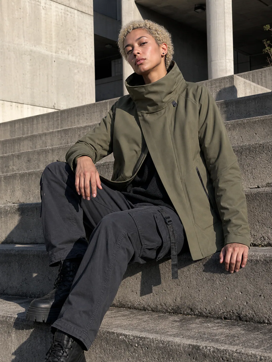 Mexico City plaza styling image showing the olive Clothixpack CXP-J111 Pilot Hardshell Jacket with a black mesh base layer and charcoal cargos.